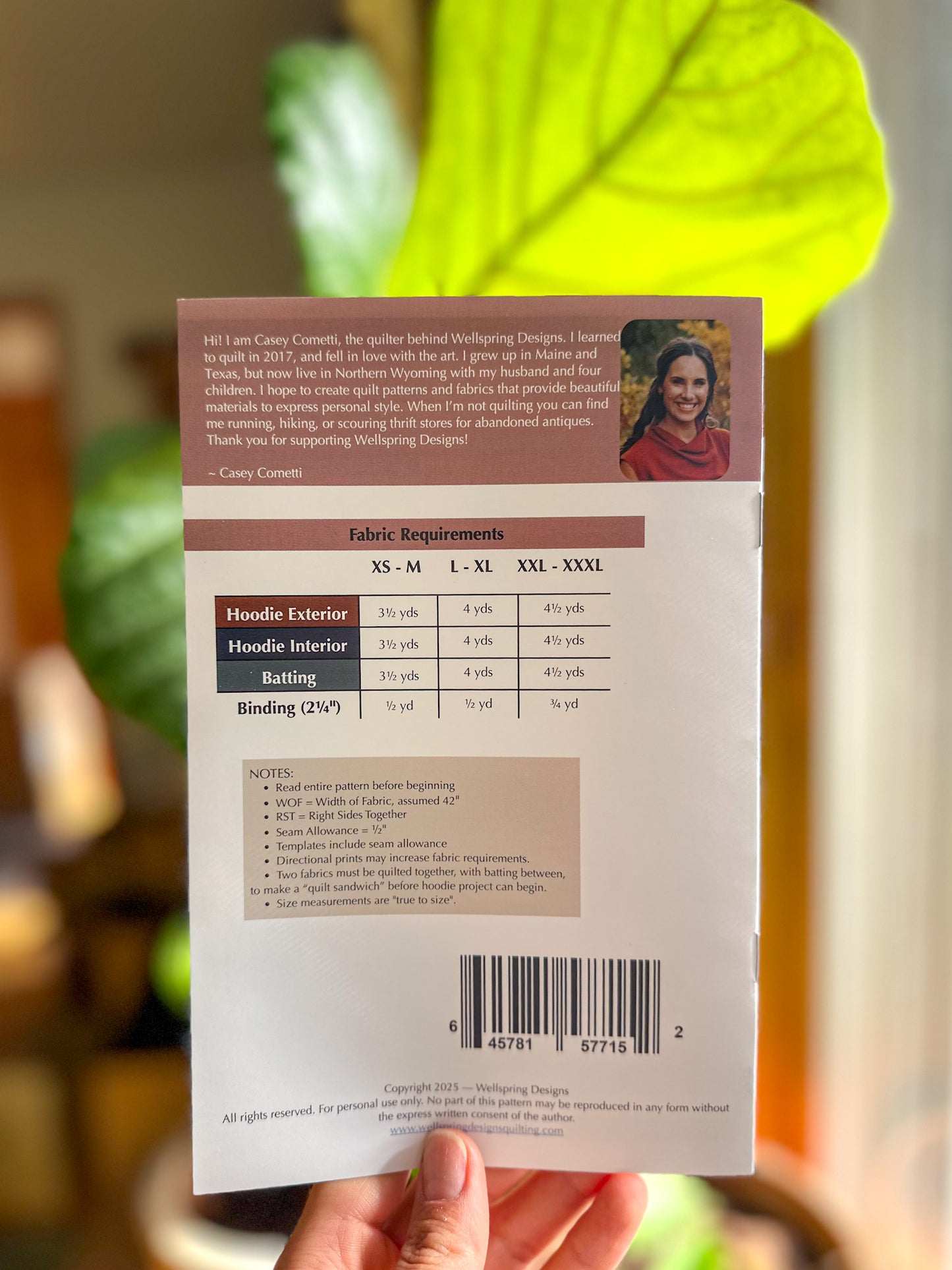 Back of a product packaging with text and a barcode, held in front of a blurred green plant.