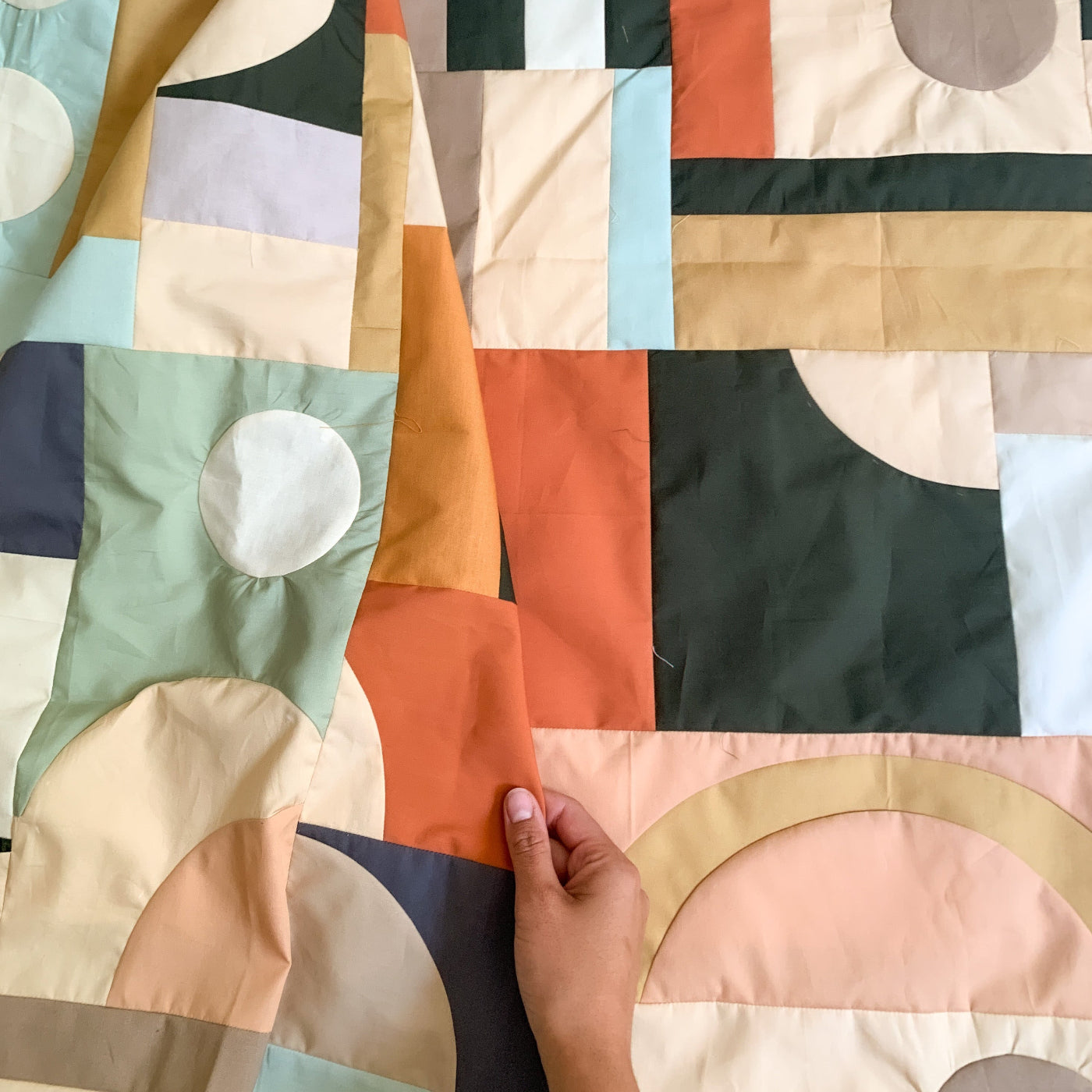 Colorful quilt with geometric patterns and a hand touching it