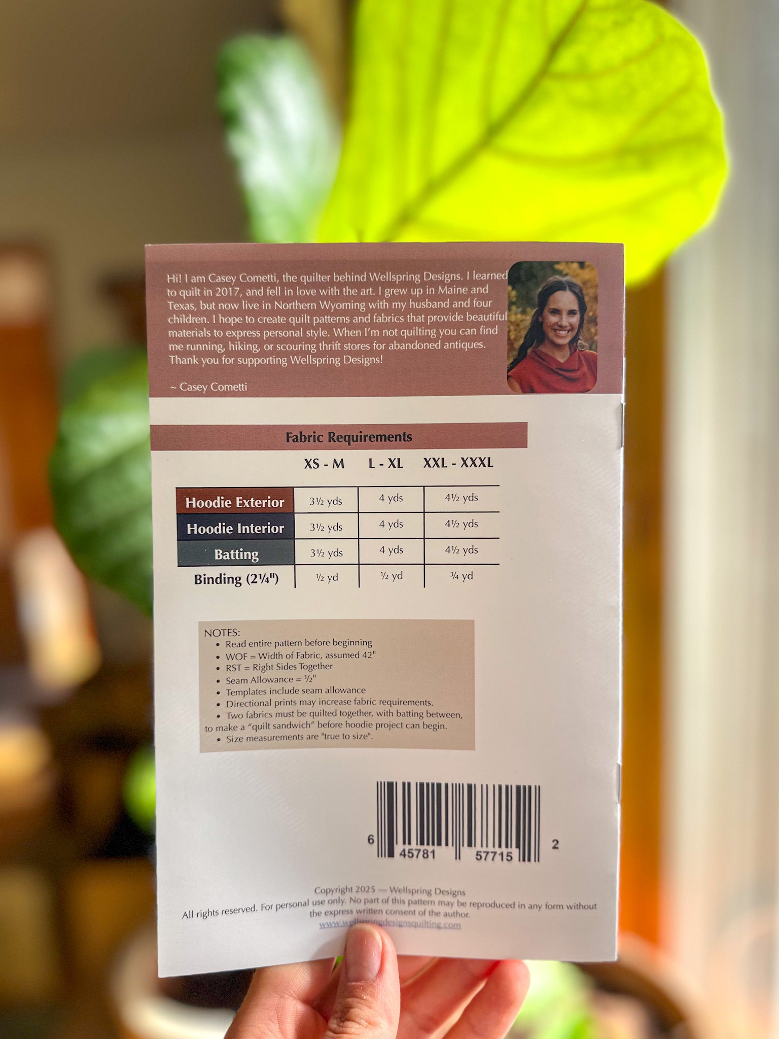 Back of a product packaging with text and a barcode, held in front of a blurred green plant.